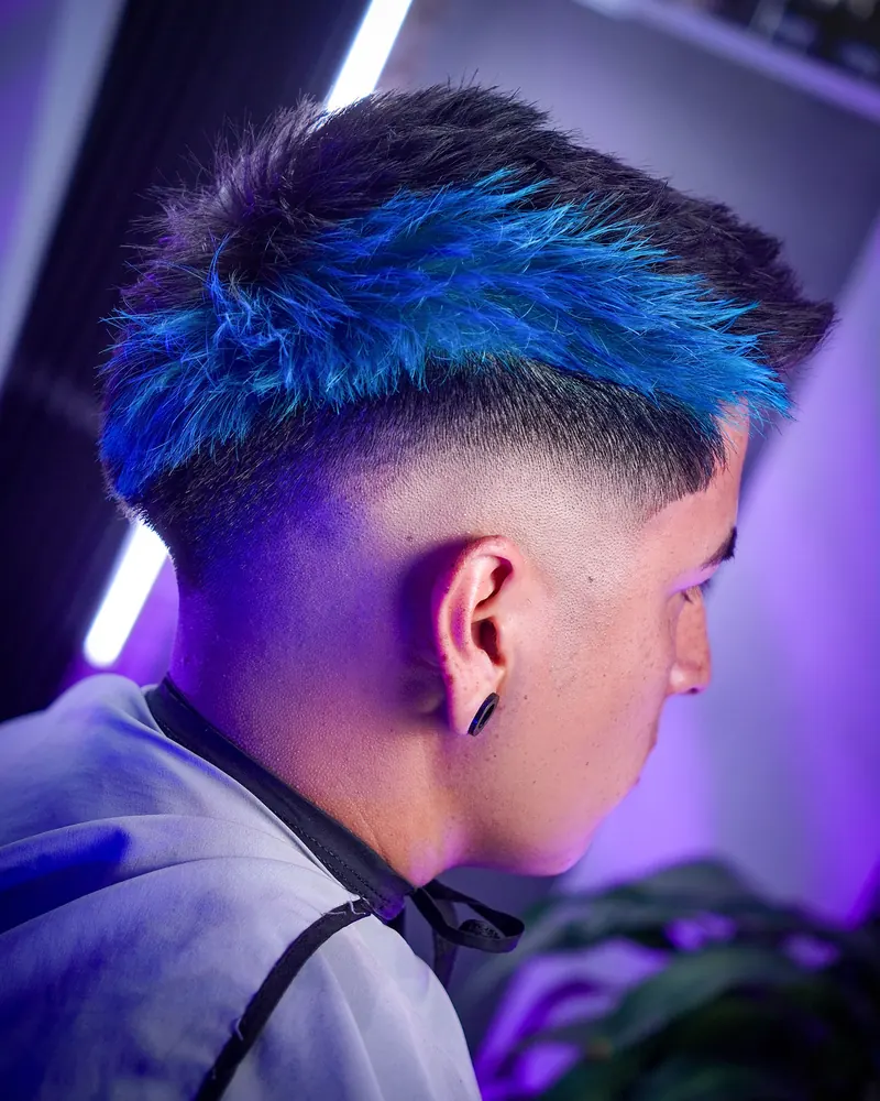 Low fade con mechas azul eléctrico en la parte superior, vista de nuca